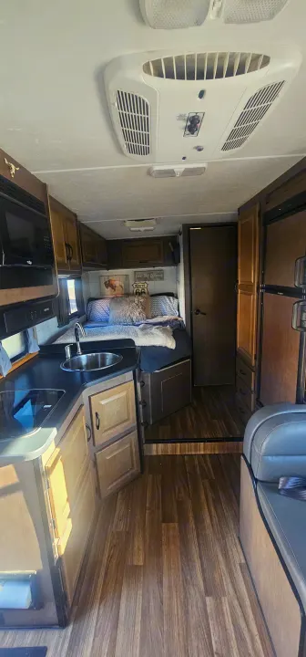 Inviting RV rental interior with kitchen, bed, and living area, featuring wood-look flooring and cabinets.. Thor Majestic 2019