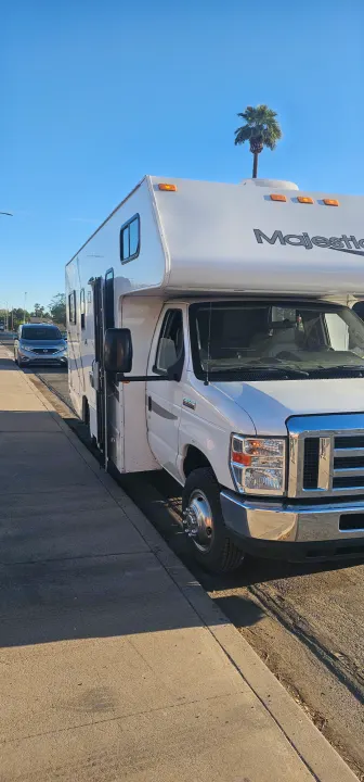 Sunny view of a white Majestic RV rental, a Class C motorhome, parked on the street next to a sidewalk.. Thor Majestic 2019