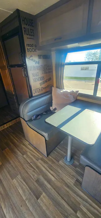 Cozy rv rental dinette with "House Rules" sign, comfy benches, and wood flooring. Ideal for road trip memories.. Thor Majestic 2019