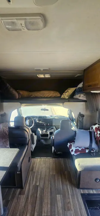 View from the back of an rv rental showing the forward living area, including the cab, overhead bunk bed, and seating.. Thor Majestic 2019