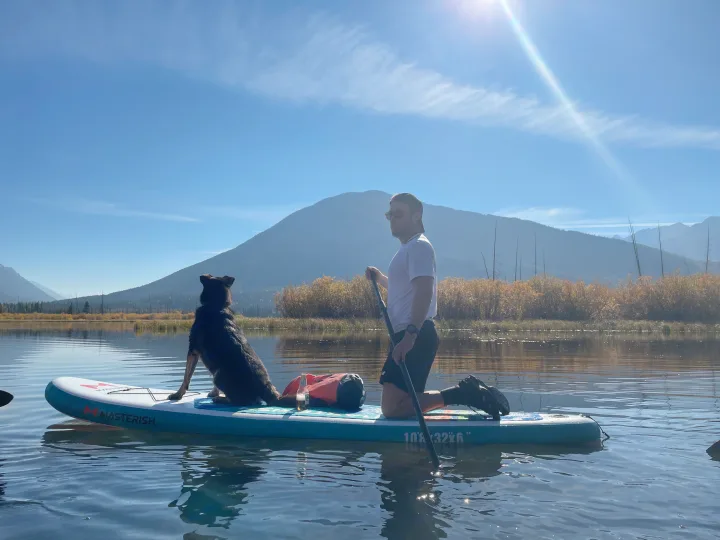 Paddleboarding with a man and his dog on a clear lake, surrounded by mountains. Great RV rental idea!. Toyota Tacoma 2020