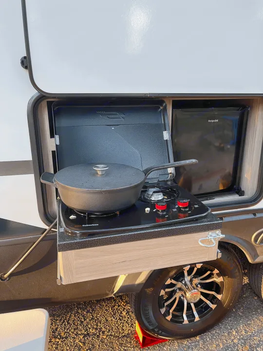 RV rental with an outdoor kitchen featuring a gas stove and cast iron pot cooking alongside a mini-fridge, ideal for camping.. Keystone RV Passport GT 2022