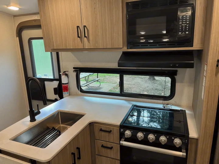 RV rental kitchen interior: modern sink, black faucet, High Pointe microwave, stove, and light wood cabinetry.. Keystone RV Passport GT 2022