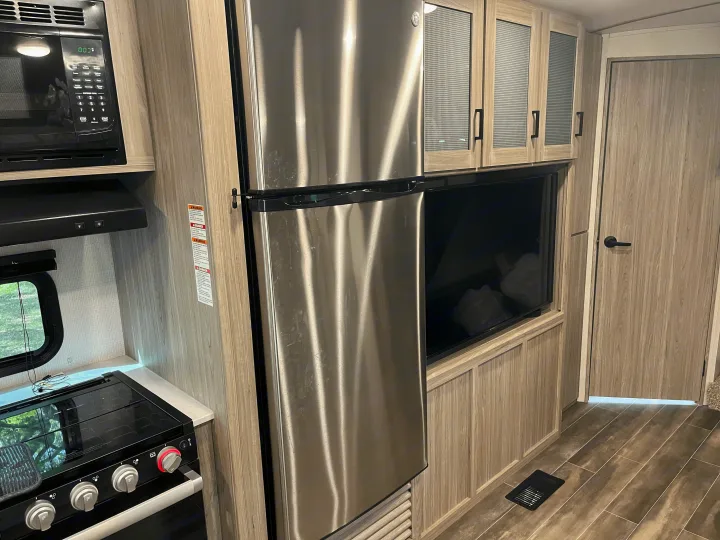 Inside an RV rental: a modern kitchen features a stainless steel fridge, microwave, stove, and cabinets.. Keystone RV Passport GT 2022