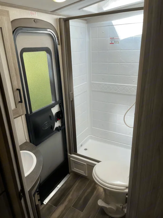 Compact RV rental bathroom features: shower, toilet, sink, and main entry door with an EXIT sign overhead.. Keystone RV Passport GT 2022