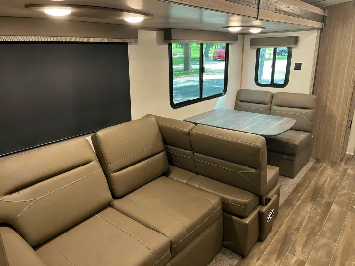Spacious RV rental interior featuring a modern sofa, dinette with table, and large windows with outdoor views.. Keystone RV Passport GT 2022