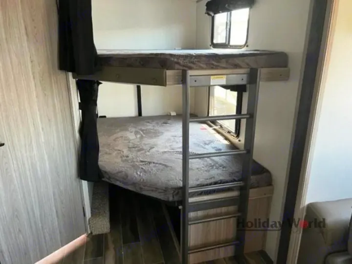 Comfortable RV rental bunk beds, ideal for family travel. Features a ladder, windows, and privacy curtain.. Keystone RV Passport GT 2022