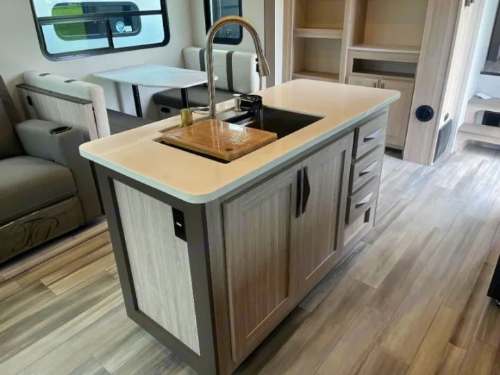 Explore this bright rv rental interior, featuring a modern kitchen island with a sink, a dining booth, and comfortable recliner seating.. Cruiser RV Essence 2025