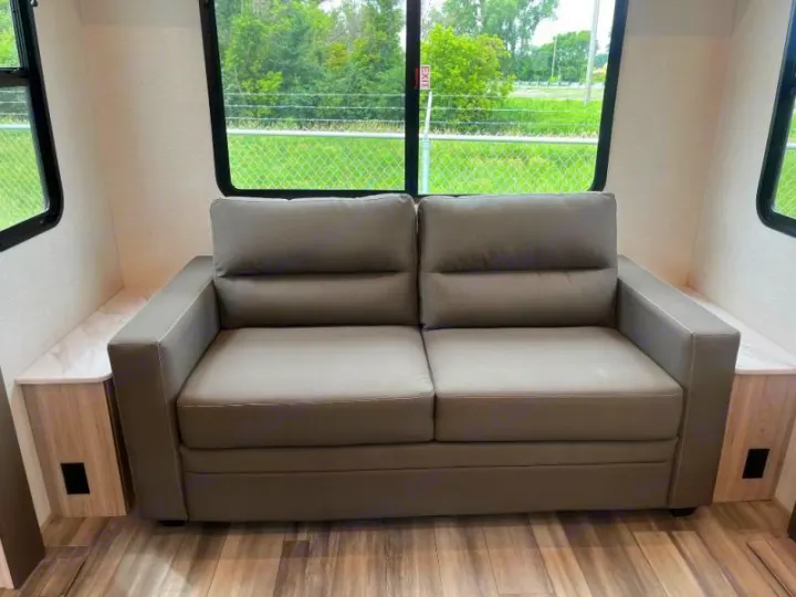 Inside an RV rental: A modern gray two-seater sofa by windows, flanked by side tables, offering a cozy spot to relax.. Cruiser RV Essence 2025