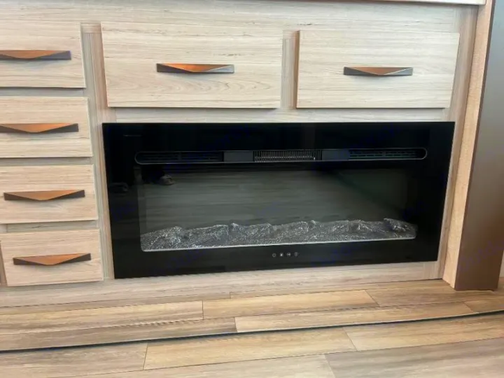 RV rental interior featuring a sleek built-in electric fireplace with an artificial log display, integrated into a modern cabinet with stylish storage drawers.. Cruiser RV Essence 2025