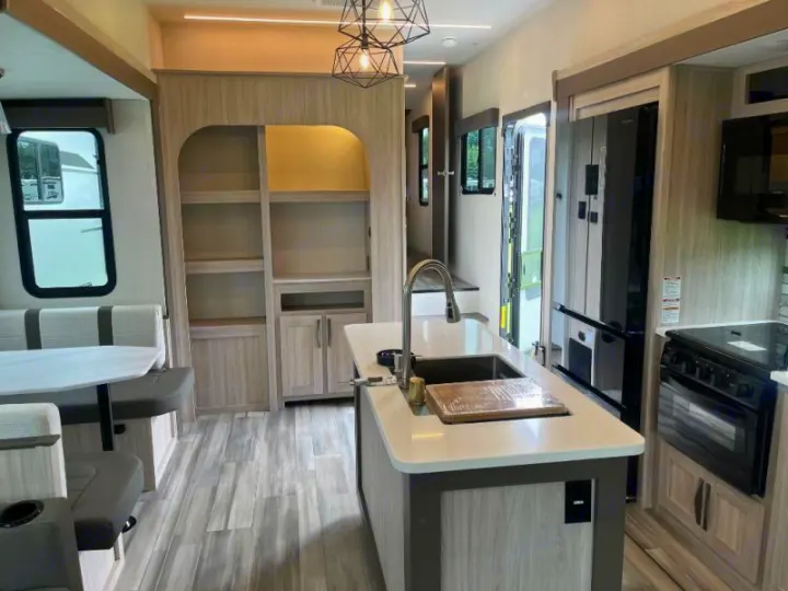 Explore this RV rental's modern interior: kitchen with island sink, dining booth, and built-in shelves on wood-look floors.. Cruiser RV Essence 2025