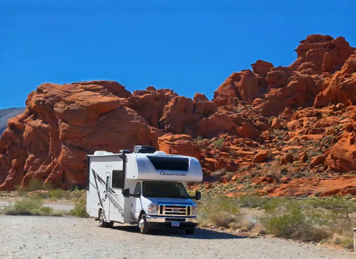 White Quantum RV rental parked against a backdrop of striking red rock formations and desert brush under a clear blue sky.. Thor Quantum 2025