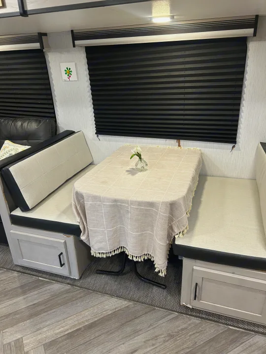RV rental dinette: cozy benches, a checkered tablecloth with a vase & flower, black privacy blinds, & wood-look floor.. Heartland RVs Mallard 2023