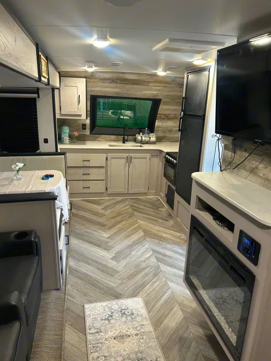 Explore this spacious RV rental interior: a modern kitchen, dining booth, and living area with a TV and electric fireplace.. Heartland RVs Mallard 2023