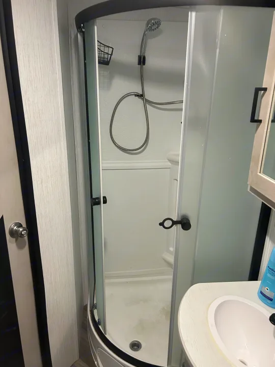 Modern compact bathroom in an rv rental. It features a curved glass shower with a handheld showerhead, sink, and stylish decor.. Heartland RVs Mallard 2023