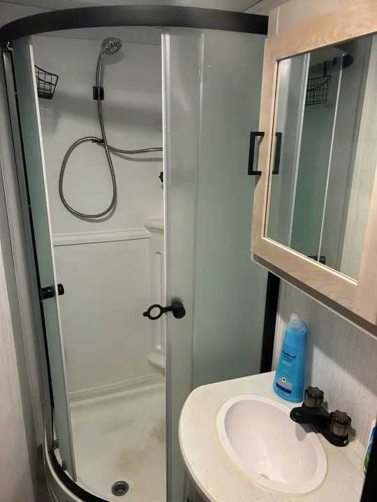 This RV rental features a compact bathroom with a shower, flexible shower head, small sink, and a mirrored cabinet, ideal for travel.. Heartland RVs Mallard 2023