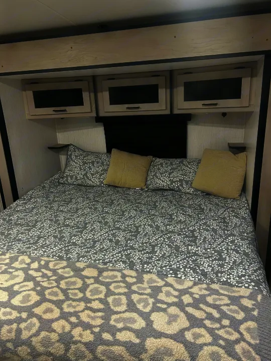 Cozy RV rental bedroom with gray patterned bed, beige pillows, and modern overhead cabinets for a compact, stylish space.. Heartland RVs Mallard 2023