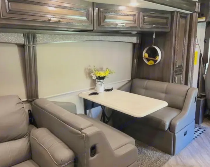 Inside an RV rental, a gray leather dinette with a white table is central, flanked by overhead wood cabinets. Flowers on the table.. Southwind Southwind Motorhome 2020
