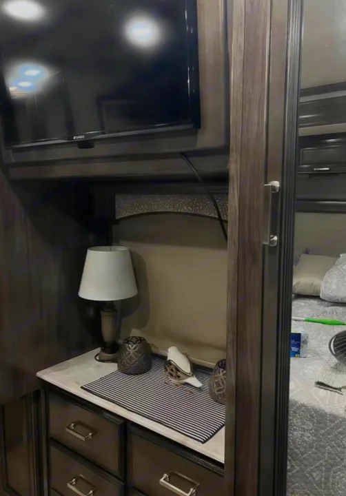 Inside a cozy RV rental bedroom area with TV, lamp, and dresser. Features smart storage, perfect for your next trip.. Southwind Southwind Motorhome 2020