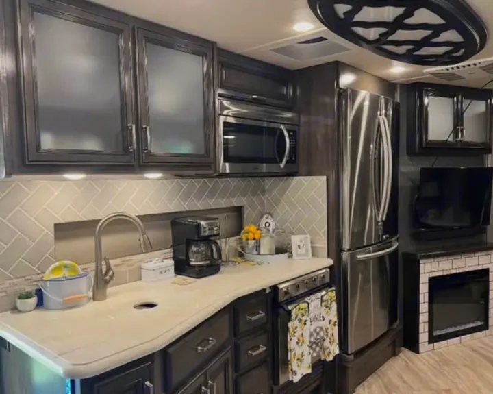 RV rental's modern kitchen: dark cabinets, stainless steel fridge/microwave, light countertop, tiled backsplash, and electric fireplace with TV.. Southwind Southwind Motorhome 2020