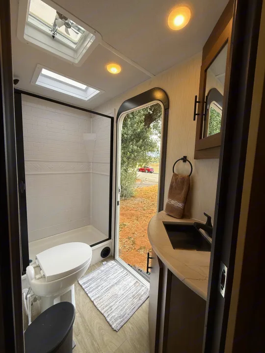 Bright RV rental bathroom with a modern shower, toilet, and vanity, featuring overhead skylights for natural light.. Forest River Wildcat One 241DBEDS 2026