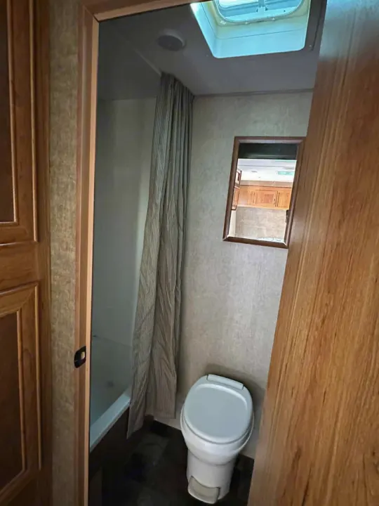 RV rental's compact bathroom features a toilet, shower with curtain, and mirror reflecting the kitchen. Bright skylight above.. Starcraft AR-One Maxx 2017