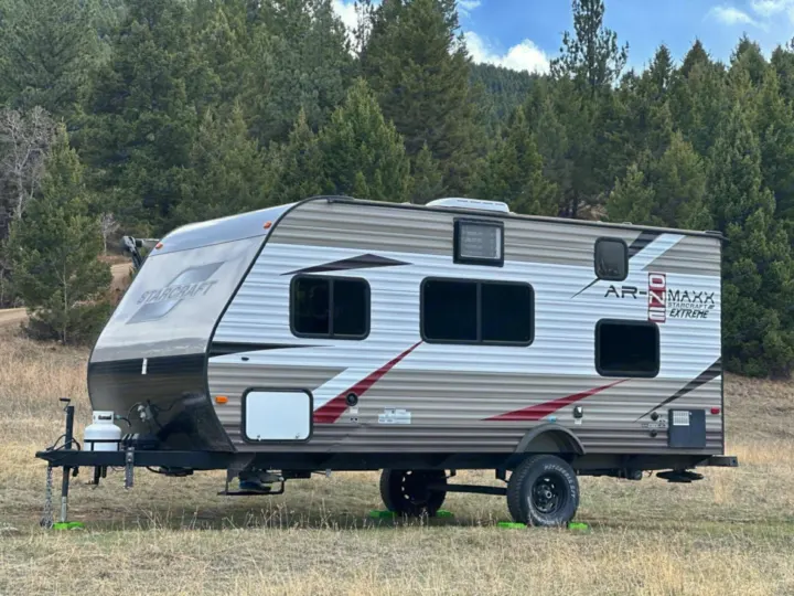 This Starcraft AR-MAXX Extreme rv rental travel trailer is parked outdoors on green leveling blocks, with a forest background.. Starcraft AR-One Maxx 2017