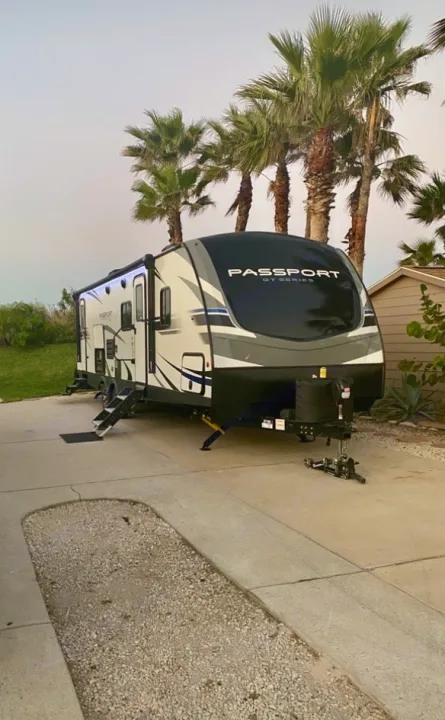 Sleek Passport GT Series travel trailer rv rental, white and black, steps down, parked on concrete under palm trees for vacation.. Keystone RV Passport GT 2021