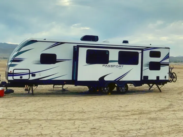 This RV rental is ready for adventure, parked on a dry lake bed under a cloudy sky. Perfect for camping.. Keystone RV Passport GT 2021