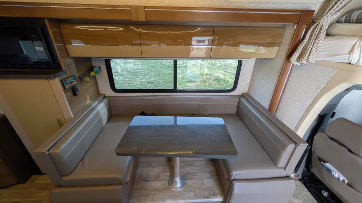 Rv rental interior: a comfy booth dinette with a table, kitchen microwave, and overhead cabinets. Enjoy the outdoor view.. Winnebago View 2017