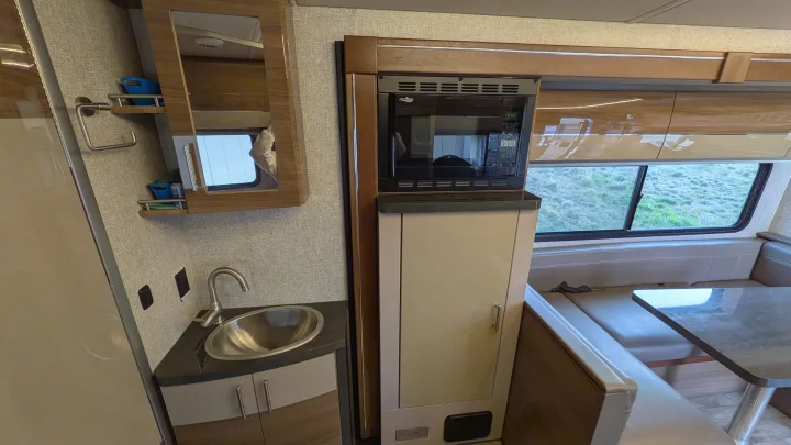 Inside this RV rental: compact kitchen/bath area with sink, mirror, microwave, and a dinette by the window for scenic views.. Winnebago View 2017