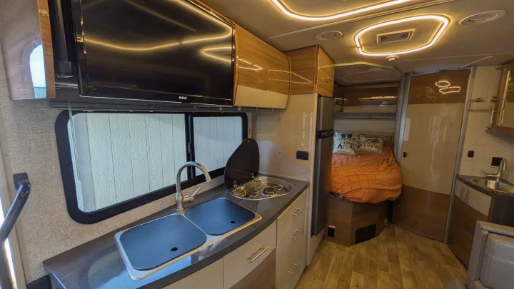 Cozy and modern rv rental interior featuring a compact kitchen, TV, comfortable bed, and stylish cabinetry.. Winnebago View 2017