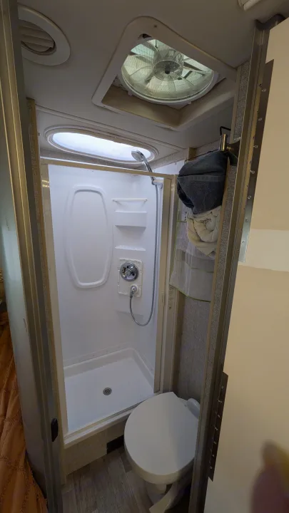 Compact RV rental bathroom with a stand-up shower, toilet, ceiling vent fan, and bright skylight.. Winnebago View 2017