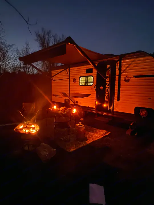 Cozy night camping with an RV rental. Pioneer RV, campfire, lanterns, and outdoor seating under the dark blue sky.. Heartland RVs Pioneer 2025