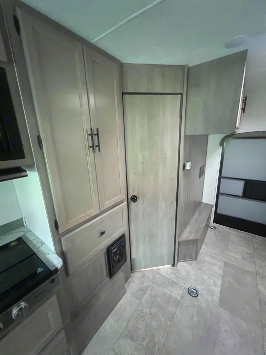 RV rental: compact kitchen area featuring light wood cabinets, stovetop, modern flooring, and entry bench.. Coachmen Freelander 22xg 2020