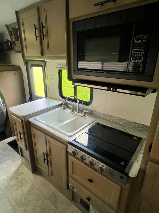 RV rental kitchen: modern microwave, sink, stove, and light cabinets with marble countertops. Ready for your next adventure.. Coachmen Freelander 22xg 2020