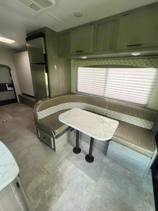 Modern RV rental interior with a U-shaped dinette, marble-look table, and patterned seating. Clean grey flooring & cabinets.. Coachmen Freelander 22xg 2020