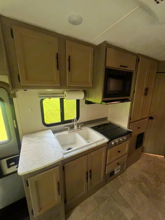 Fully equipped RV rental kitchen: double sink, stovetop, microwave, and light-colored cabinets. Ready for your adventure.. Coachmen Freelander 22xg 2020