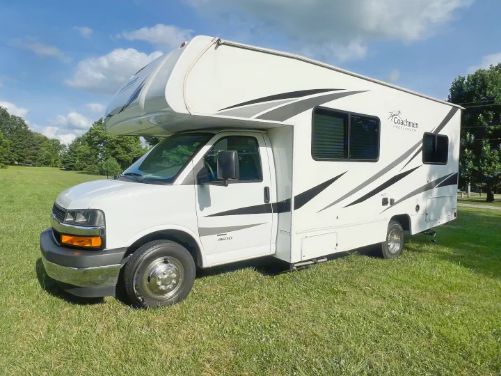 White Class C Coachmen Freelander RV rental, featuring stripe graphics, sits on green grass under a sunny, blue sky.. Coachmen Freelander 22xg 2020