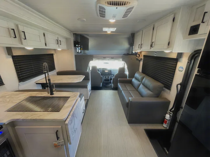 Step inside this modern RV rental's bright interior, featuring a kitchen with sink, cozy dinette, and a spacious sofa.. East to West Entrada 2024