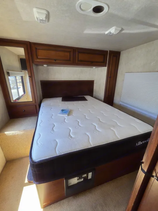 Spacious RV rental bedroom featuring a queen bed with an Allswell mattress, built-in storage, and window. Ready for adventure.. Jamboree Sport 2010