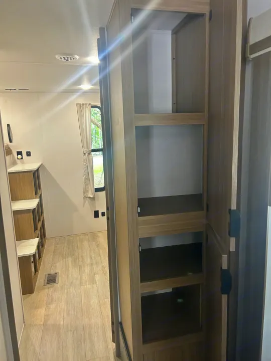 RV rental interior showcasing an open storage closet with shelves, complemented by a modular storage unit and window.. Forest River Wildwood 2025