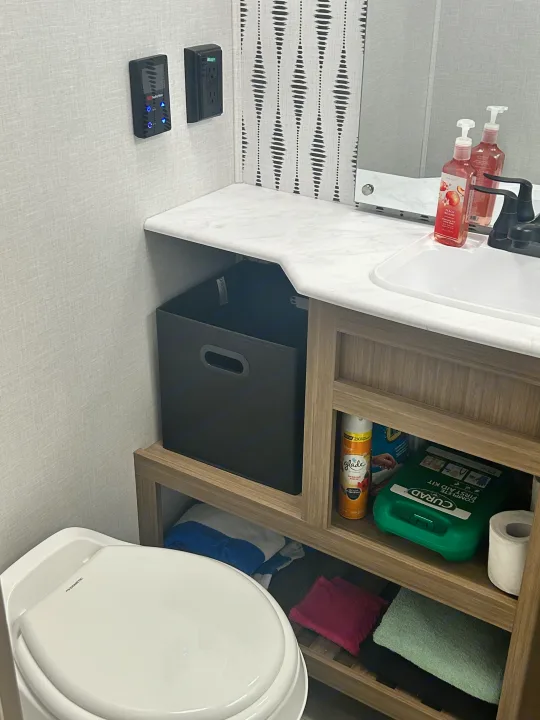RV rental bathroom showing a toilet, sink vanity with soaps, and practical storage for towels & first aid kit.. Forest River Wildwood 2025