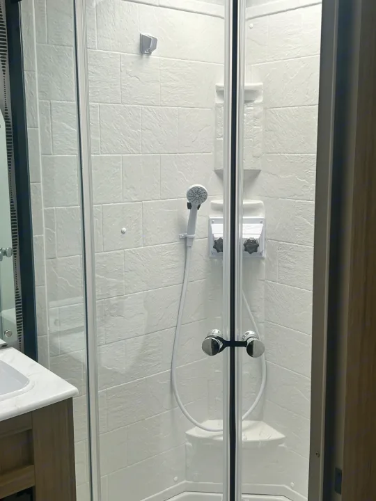 RV rental: View inside a bright, compact shower featuring clear glass doors, white tiled-look walls, a showerhead, and controls.. Forest River Wildwood 2025