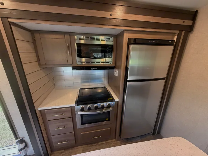 RV rental kitchen with stainless steel microwave, oven, and refrigerator. Light wood cabinets, speckled countertop, and tiled backsplash.. Crossroads RV Sunset Trail 2021