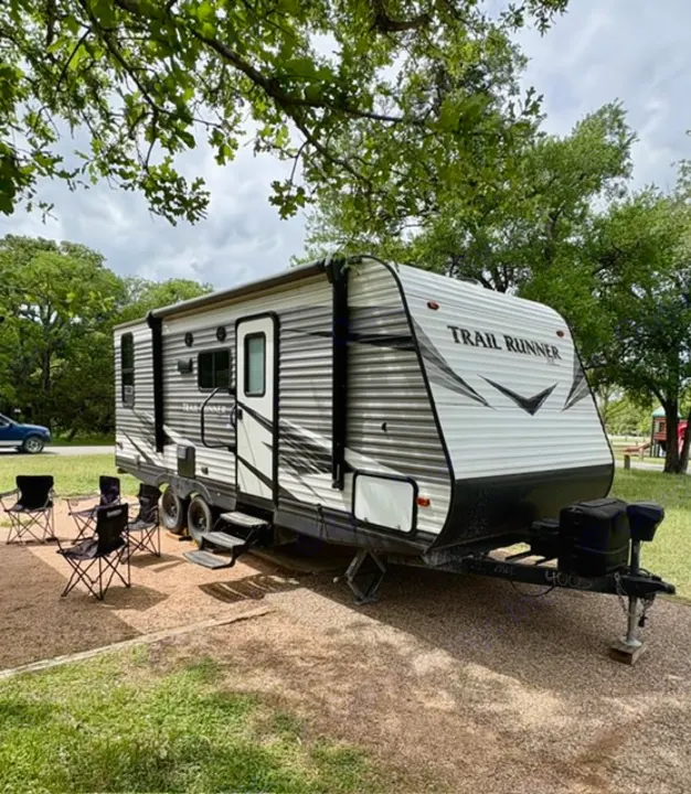 This Trail Runner rv rental is ready for adventure! Parked at a scenic campground with chairs & an awning for outdoor relaxation.. Heartland RVs Trail Runner SLE 2019