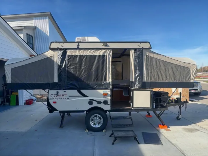 Fully set up pop-up camper, an ideal RV rental. This beige & black folding trailer is expanded, showing windows & steps.. Starcraft Comet 2016