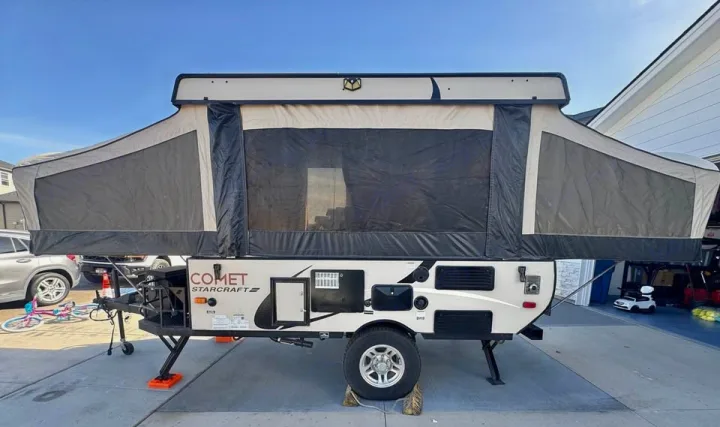 Pop-up camper RV rental: A beige and dark grey Comet Starcraft model with extended tent sections, parked on a driveway.. Starcraft Comet 2016