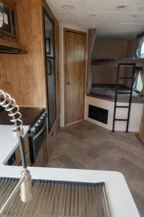 RV rental interior featuring a kitchen with sink, stove, microwave, and fridge, plus bunk beds with a ladder.. Palomino Other 2022