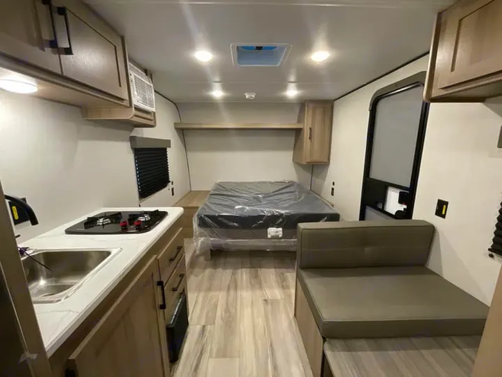 RV rental interior: A compact living space featuring a kitchenette with sink & stove, a bed, and a cushioned seating area.. Keystone RV Coleman 2025
